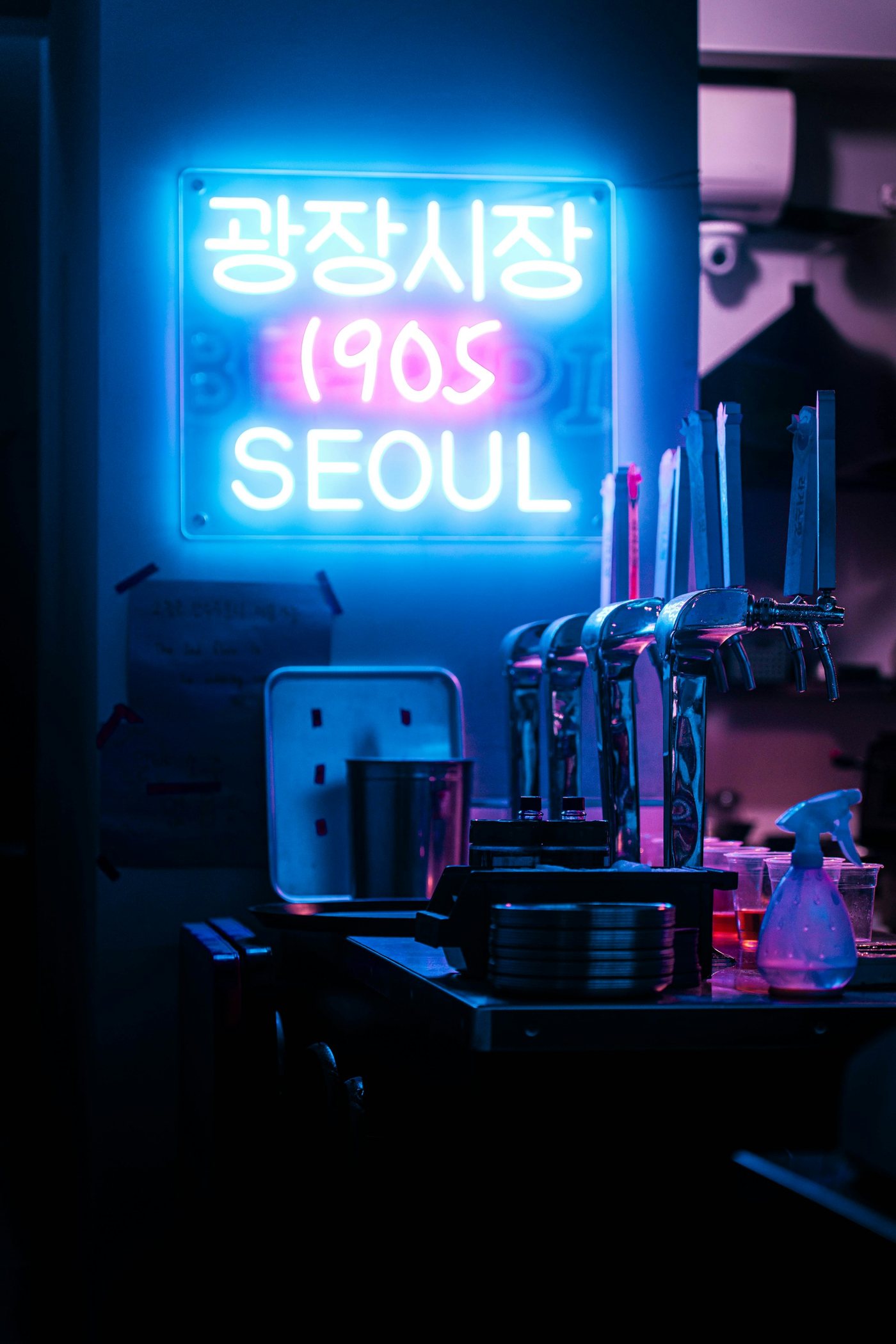 A neon bar sign glowing blue and pink above tap handles in a Seoul bar